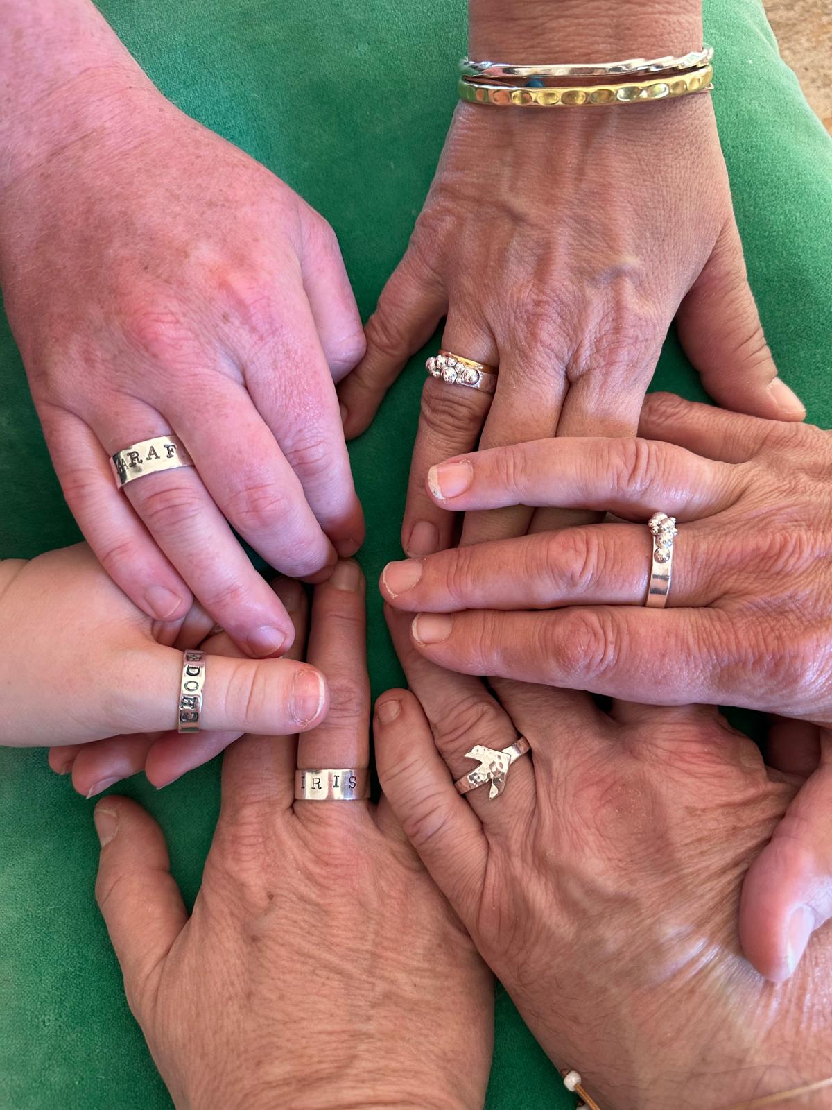 Multiple hands showing finished sterling silver rings made in the workshop